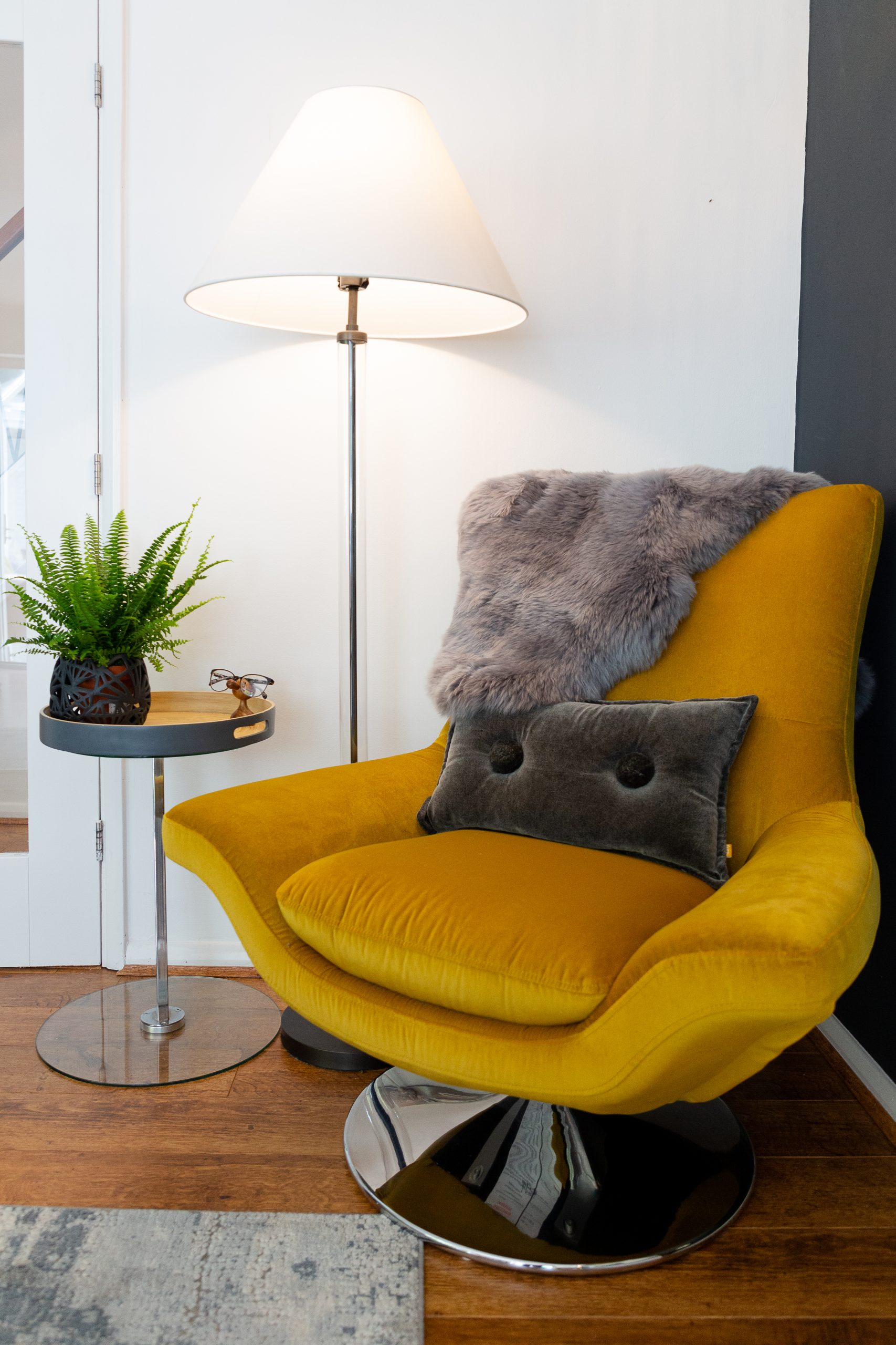 Close up image of the corner of a room featuring a bright yellow swivel armchair with a brown cushion and fur effect throw.