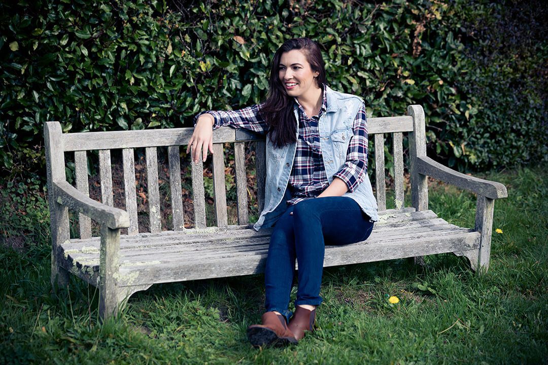 A young woman is resting on a bench in the countryside. An example of a corporate portrait on location.