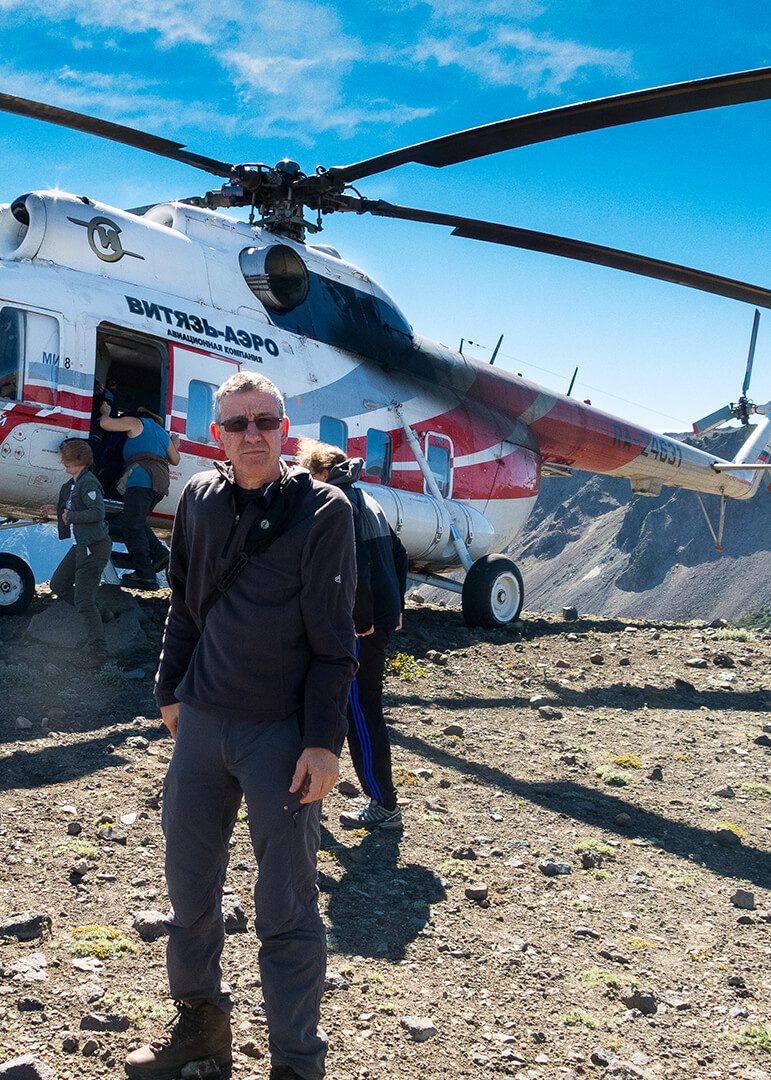 Photographer Andrew Boschier standing in front of a Russian helicopter on th erim of a volcano in Kamchatka.