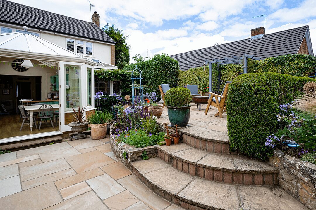 A view of a garden patio with curved steps leading to a seating area and pergola. An w=example of garden design photography.