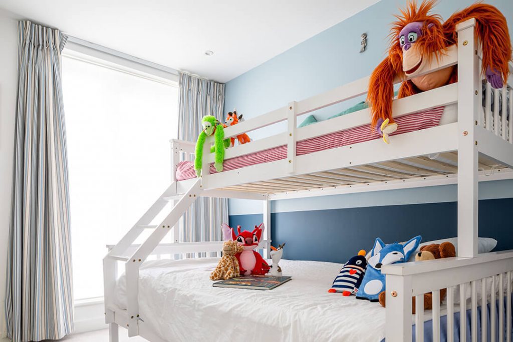 A view of a childs bedroom with bunk beds. There are cuddly toys arranged on the bedding