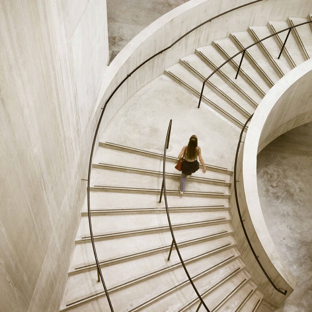 An overhead view of the concrete staircase in the Blavatnik Building in the Tate Modern. A young woman is halfway up the stairs