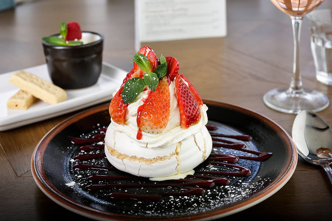 A tasty looking strawberry pavlova with a sprig of mint with a lemon posset in the background.