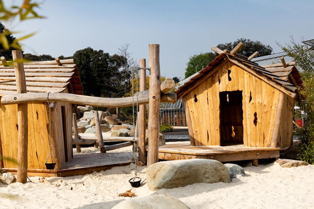 A number of wooden huts surrounded by sand in a play area in the new childrens garden at Kew.