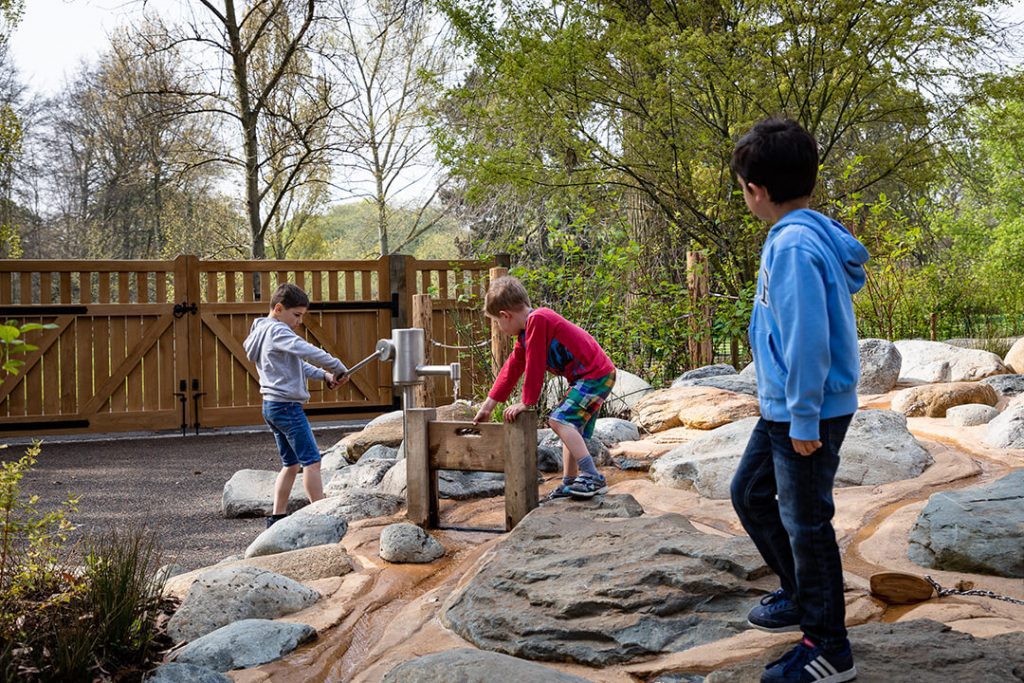 A group of children enjoying the water garden at the childrens garden at Kew. There are water pumps and sluices to play with.