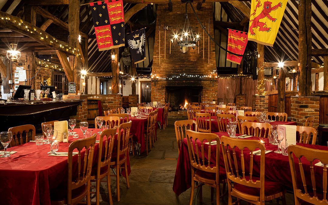 A very atmospheric image of the medieval styled banqueting hall at the Crown and Cushion pub in Minley, Hampshire including hanging fags and suits of armour.