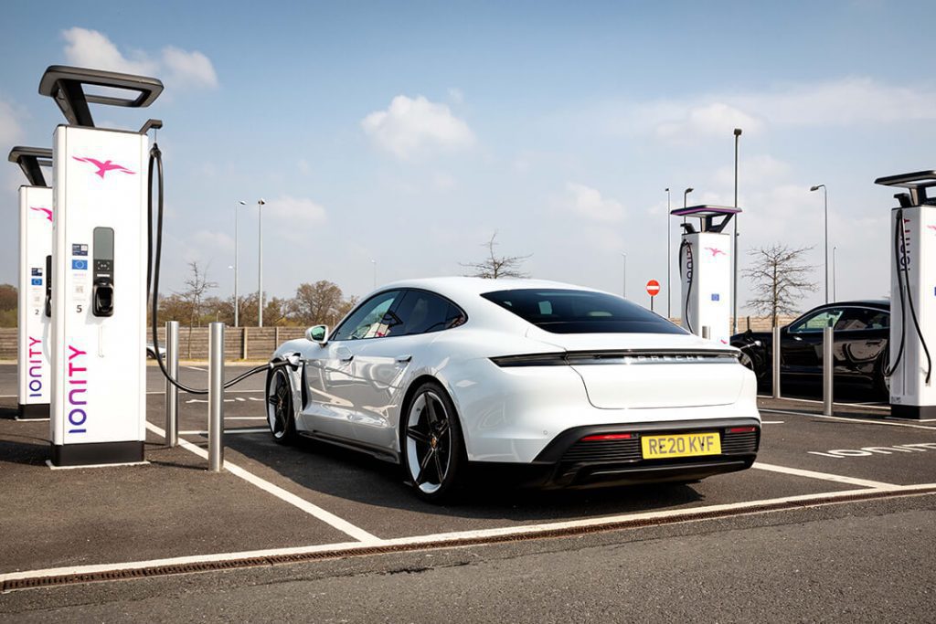 A white Porche Taycan car parked in a bay next to a high speed charging point at a motorway services