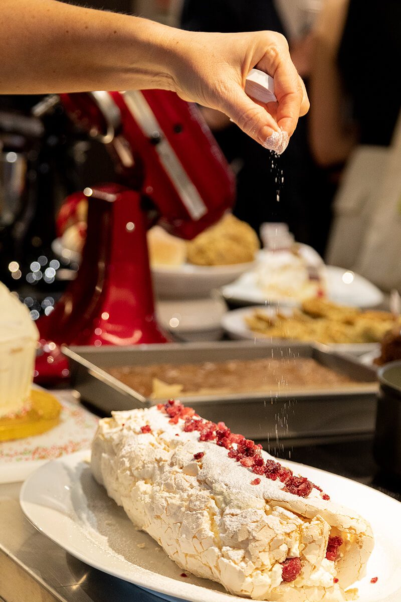 Close up of someone sprinkling sugar over a rasperry roulade in a cookery demonstration