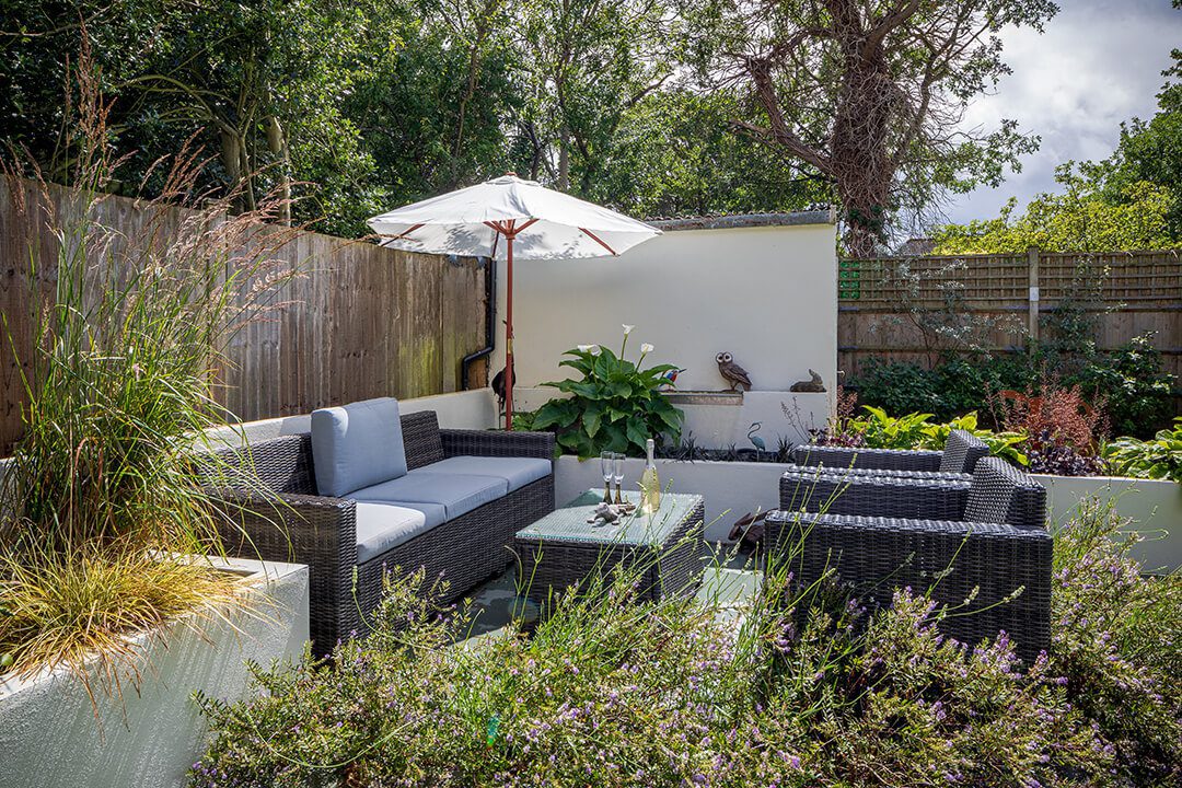 A family entertainment area in a corner of a garden surrounded by concrete planting bedsa nd a sunshade