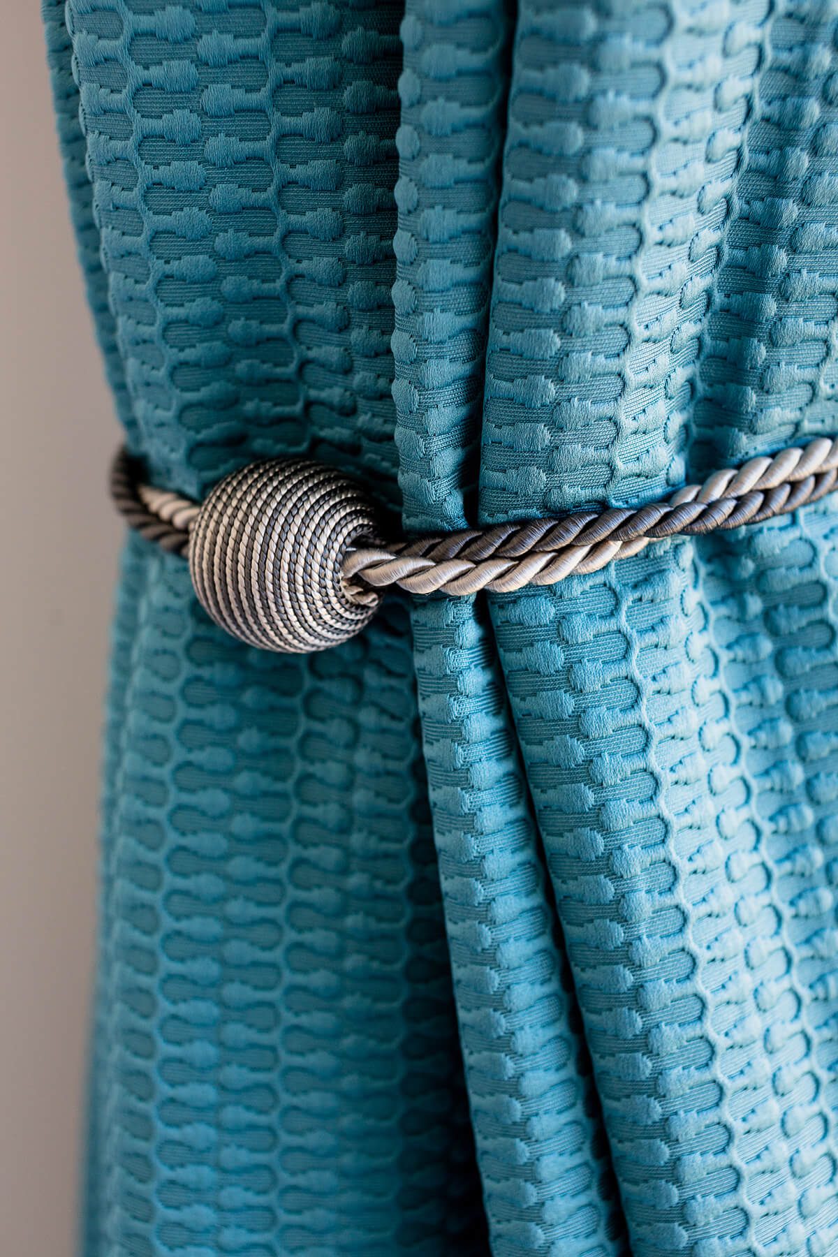 Detail of bright blue textured curtains with a silver rope effect holdback.